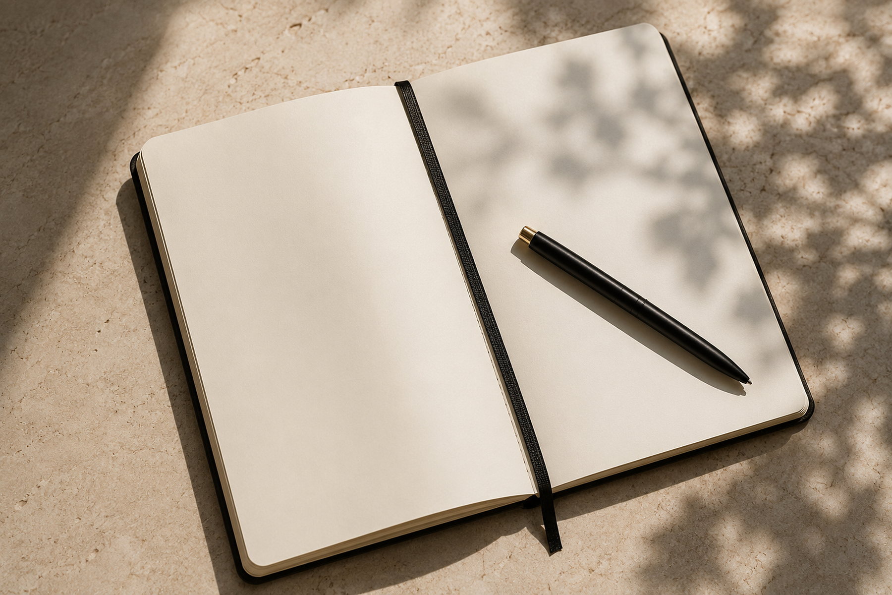 An open notebook with blank pages and a pen, on stone in dappled daylight.